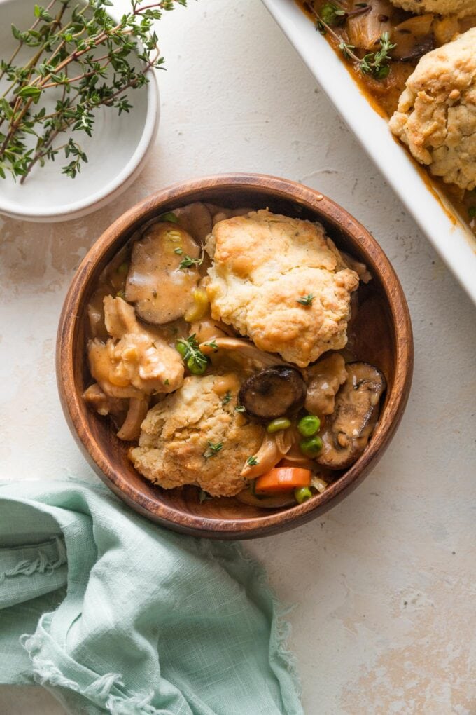 Overhead view of a bowl full of chicken pot pie with homemade Parmesan biscuits on top, with the full pan visible to the side.