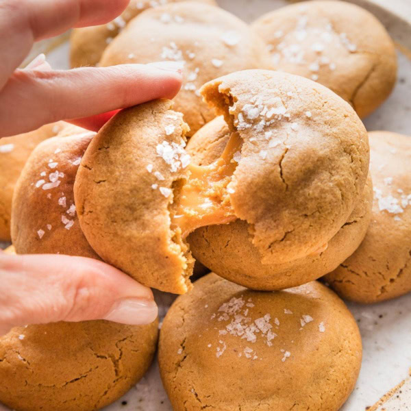 Close up of a woman's hand pulling apart a brown sugar molasses cookie to reveal a chewy caramel baked inside.