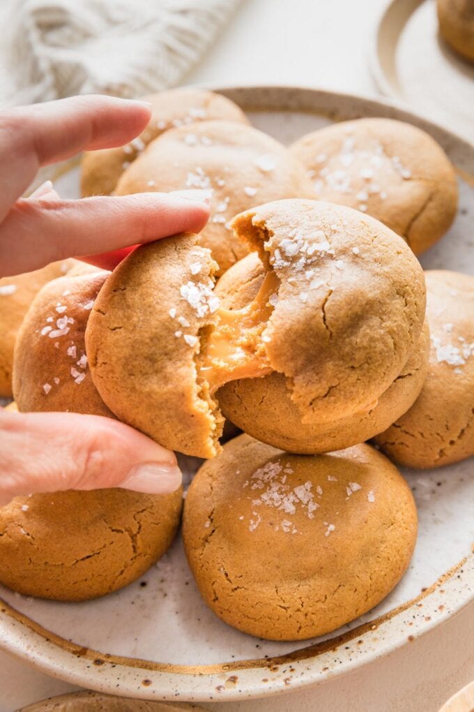 Close up of a woman's hand pulling apart a brown sugar molasses cookie to reveal a chewy caramel baked inside.