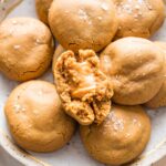 Close up image of a caramel-stuffed molasses cookie broken in half to show the chewy, stretchy caramel melted in the middle.