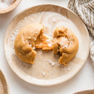 Small brown plate with a sea salt-sprinkled caramel molasses cookie on it, half pulled apart to reveal a chewy caramel inside.