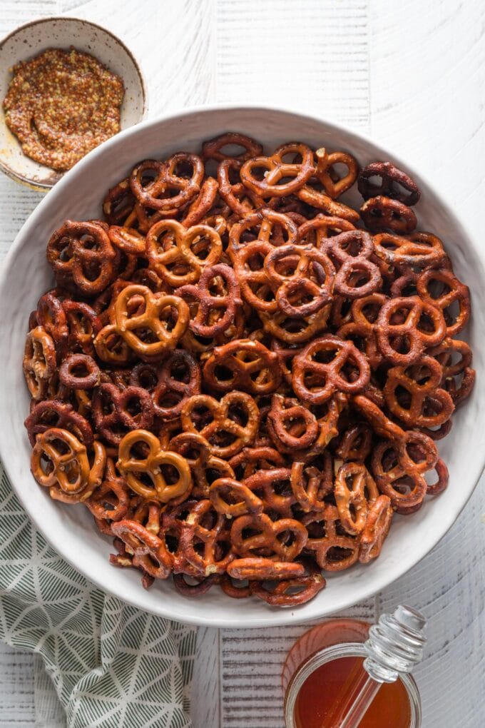 Large white serving bowl filled with homemade honey mustard pretzels, with extra honey and whole grain mustard on the countertop nearby.