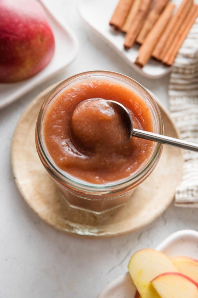 Spoon lifting a small portion of homemade apple butter out of a jar.
