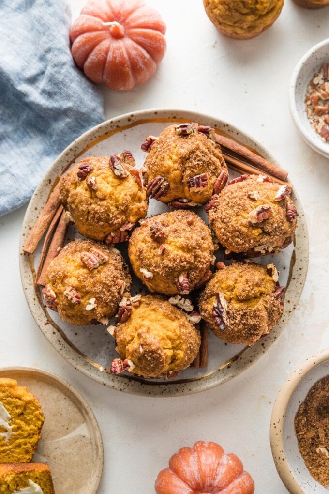 Overhead view of a plate of pumpkin muffins with pecans, surrounded by a blue cloth and decorative pumpkins.