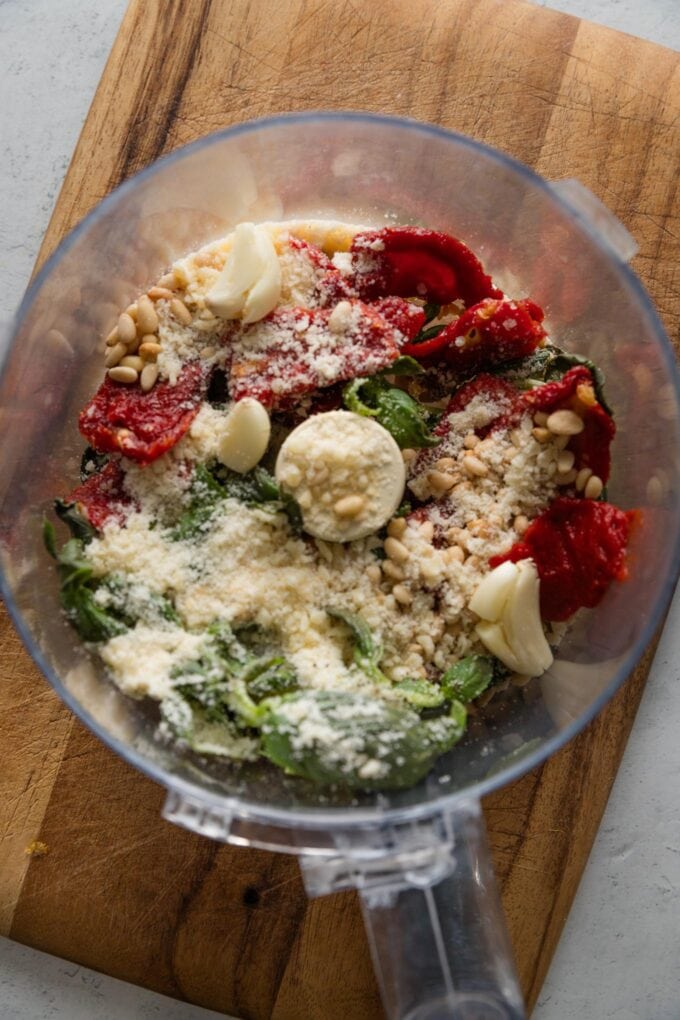 Red pesto ingredients added to the bowl of a large food processor but not yet pulsed.