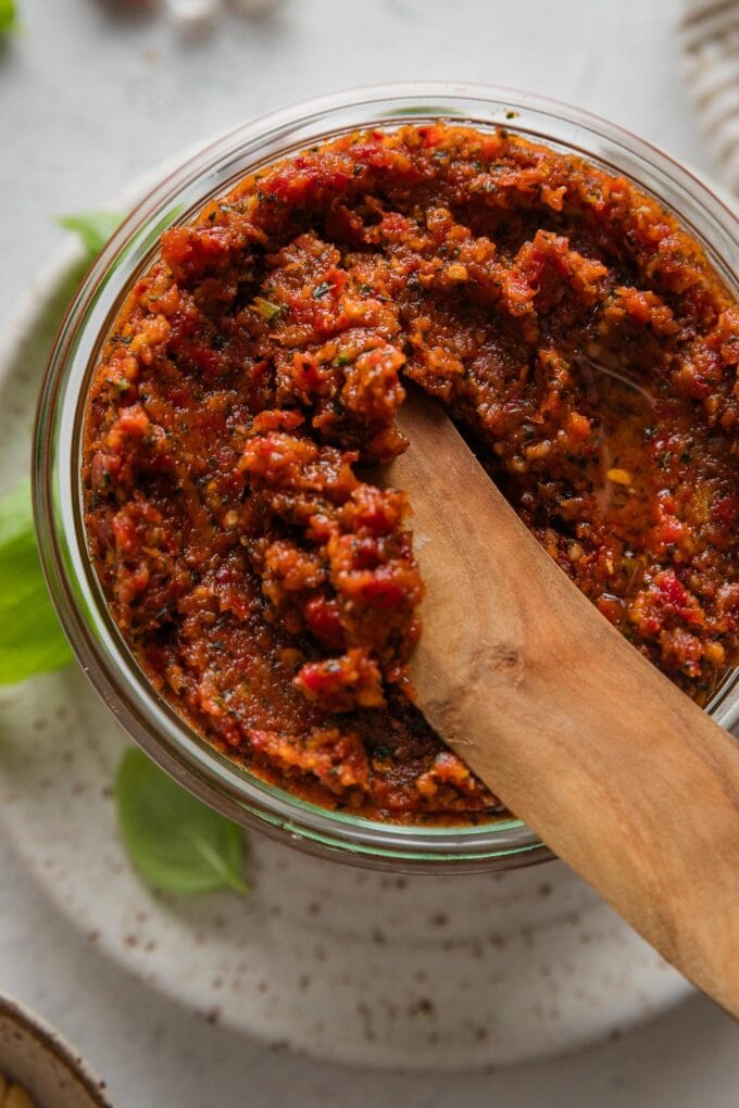 Close up of a wooden spreading knife scooping up a bit of homemade sun-dried tomato pesto.