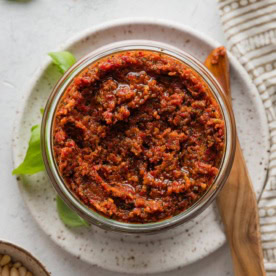 Glass jar full of homemade pesto rosso, ready to cover and store in the fridge.