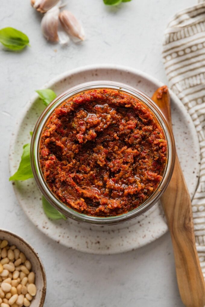 Glass jar full of homemade pesto rosso, ready to cover and store in the fridge.