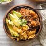 Bowl of sweet potato black bean chili served with avocado, cilantro, and corn chips.
