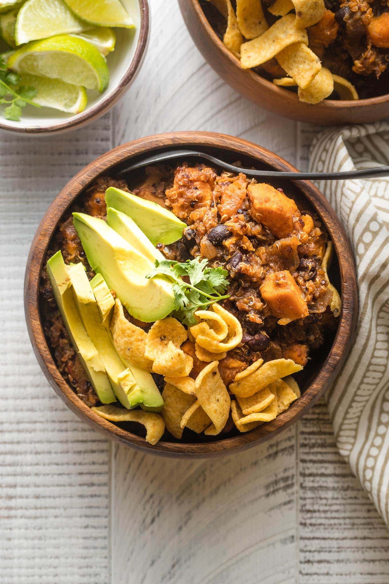 Bowl of sweet potato black bean chili served with avocado, cilantro, and corn chips.