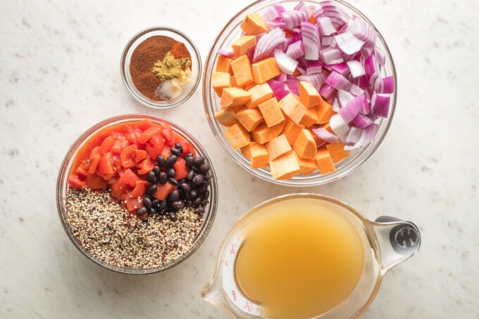 Prep bowls containing red onion, sweet potato, diced tomatoes, black beans, quinoa, veggie broth, and chili seasonings.