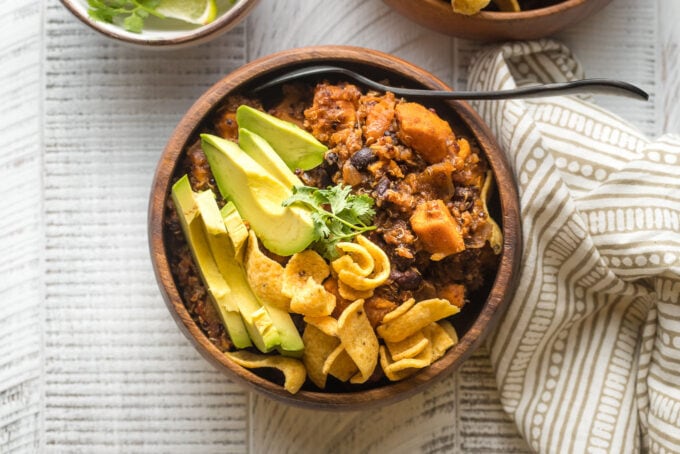 Bowl of sweet potato black bean chili served with avocado, cilantro, and corn chips.