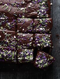 Overhead view of a dark chocolate layer cake dusted with bat and ghost themed sprinkles for Halloween and cut into small squares.
