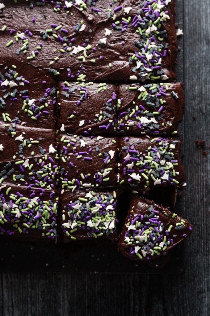 Overhead view of a dark chocolate layer cake dusted with bat and ghost themed sprinkles for Halloween and cut into small squares.