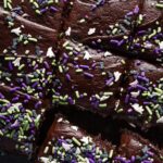 Close up overhead view of a blackout chocolate buttermilk sheet cake topped with ghost and bat-themed Halloween sprinkles and sliced into small squares.