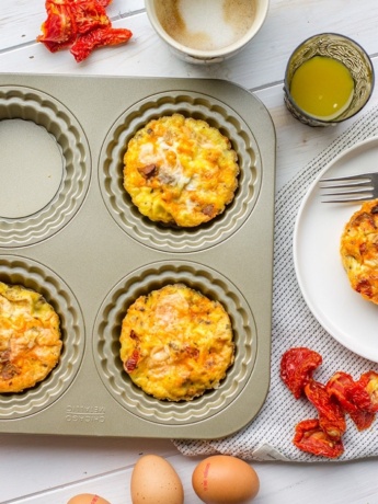 A pan of chorizo sun-dried tomato mini frittatas, surrounded by coffee, orange juice, and eggs.