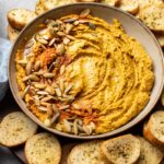 Bowl of pumpkin hummus with pumpkin seeds and paprika.