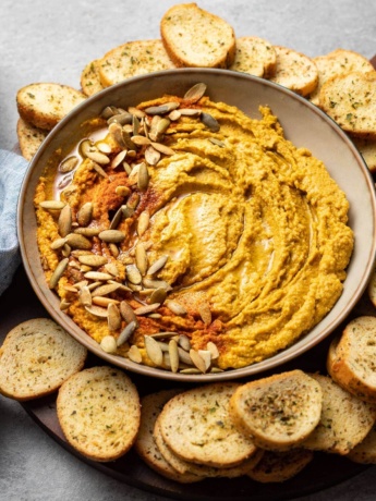 Bowl of pumpkin hummus with pumpkin seeds and paprika.