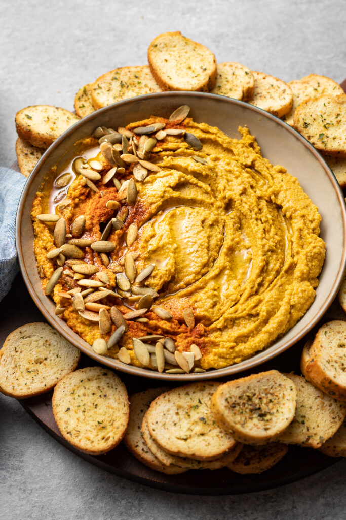 Bowl of pumpkin hummus with pumpkin seeds and paprika.