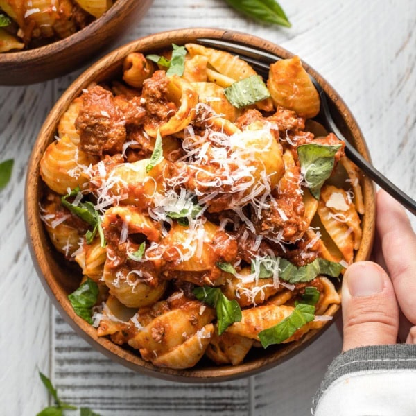 Hand holding a bowl of shells with weeknight bolognese sauce.