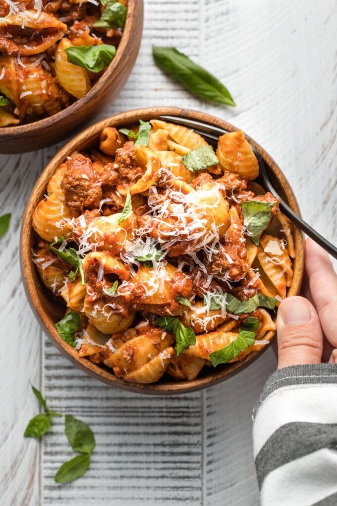 Hand holding a bowl of shells with weeknight bolognese sauce.