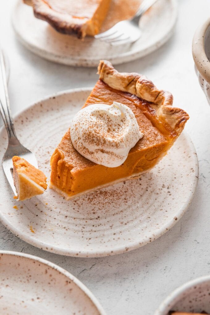 Slice of bourbon molasses-infused pumpkin pie served with whipped cream and one fork-bite taken out.