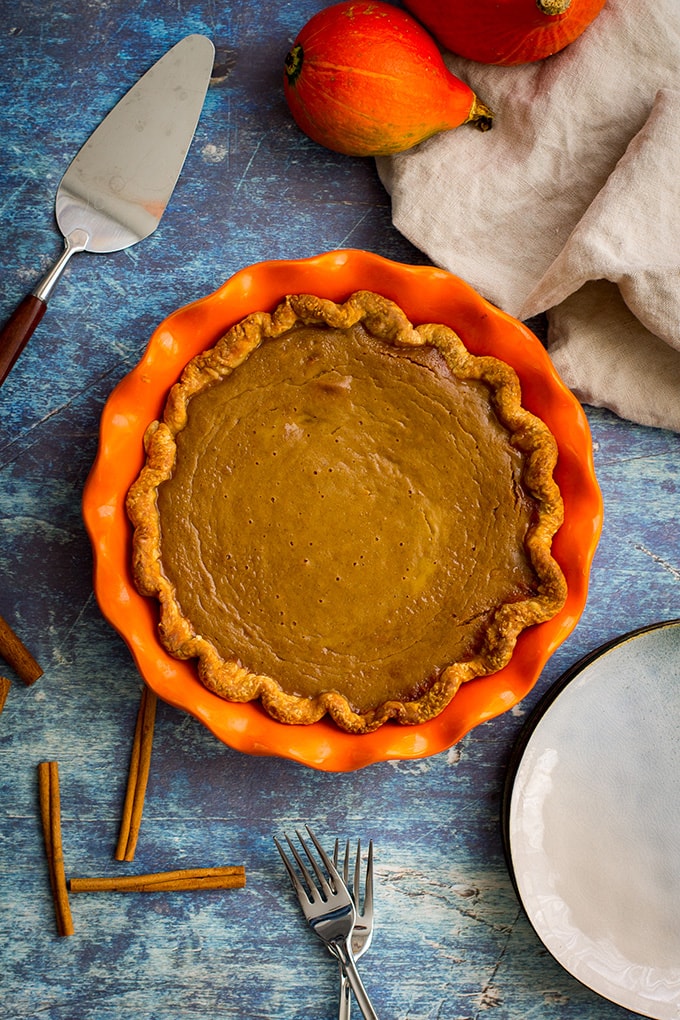 Overhead picture of bourbon molasses-spiked pumpkin pie, unsliced in an orange pie plate.