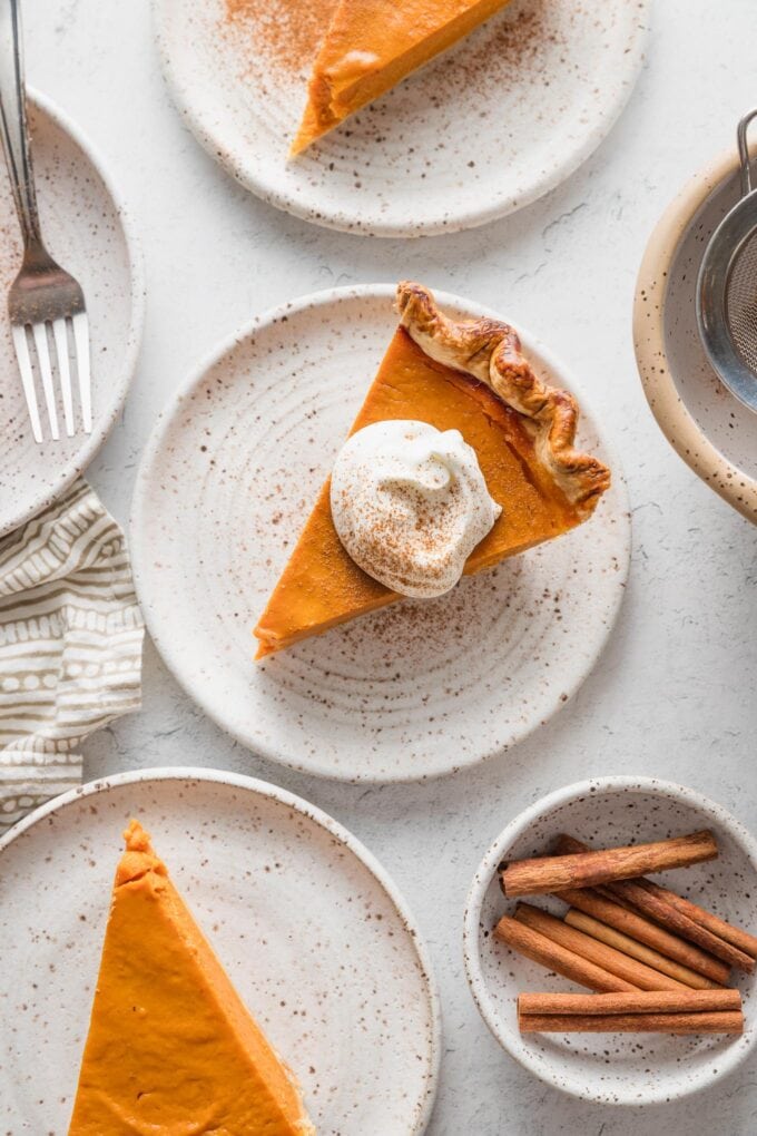 Slices of bourbon molasses pumpkin pie plated with whipped cream, ground cinnamon, and cinnamon sticks.