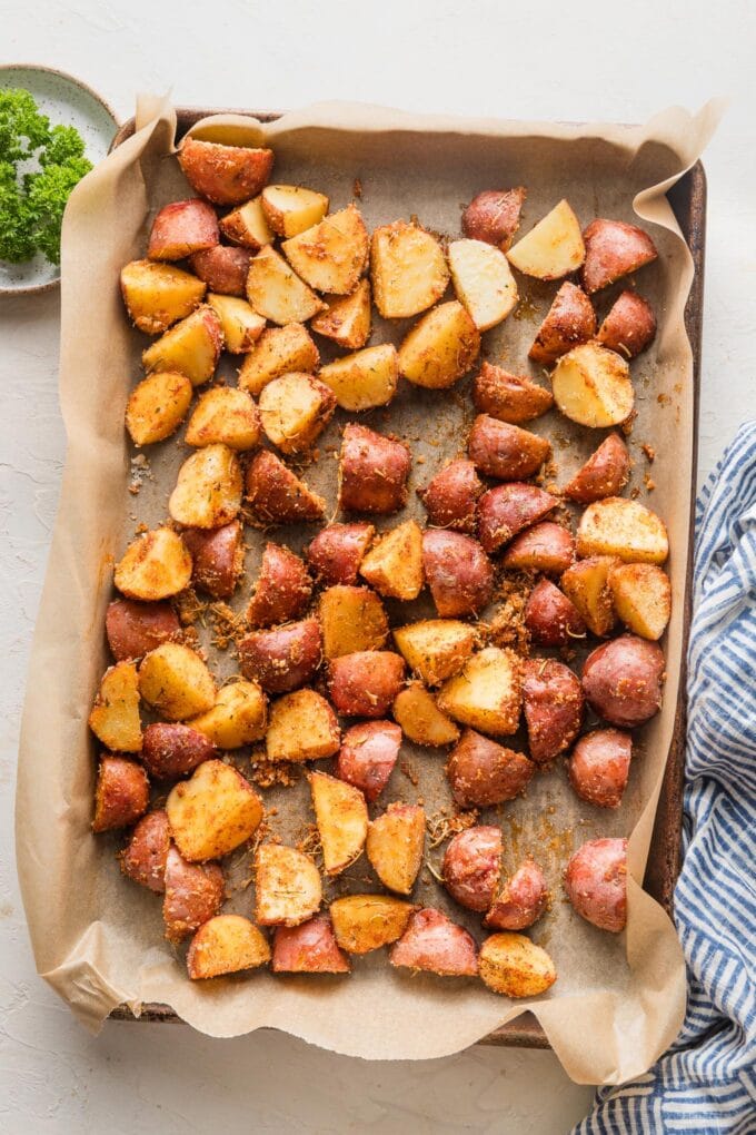 Seasoned baby red potatoes spread out on a parchment-lined baking sheet, ready to roast.