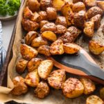 A parchment-lined sheet pan filled with roasted Parmesan crusted red potatoes, being tossed with a saute tool.