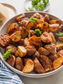 Angled view of a serving dish filled with roasted red potatoes seasoned with herbs, olive oil, and Parmesan.