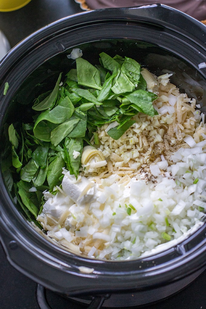 Spinach, artichokes, mozzarella, cream cheese, chopped onion, and seasonings, all in the crockpot and ready to go for a skinny spinach artichoke dip.