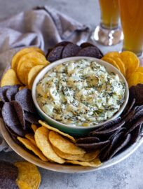 A bowl of skinny crockpot spinach artichoke dip served with tortilla chips and cold beer.