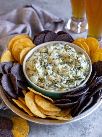 A bowl of skinny crockpot spinach artichoke dip served with tortilla chips and cold beer.