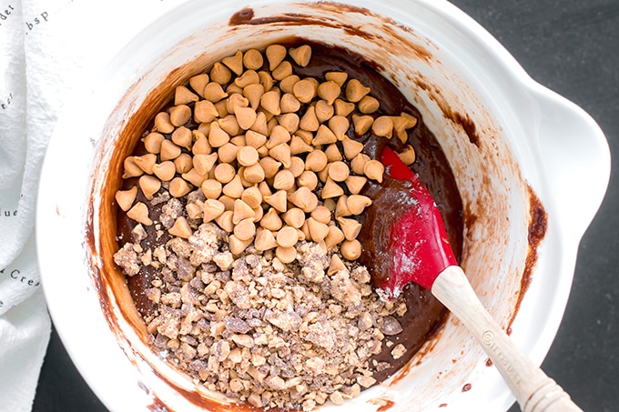 Mixing bowl filled with chocolate brownie cookie batter, butterscotch chips, and toffee bits.