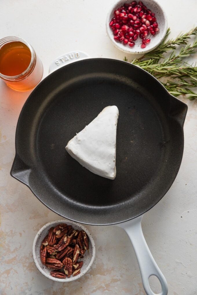 Wedge of brie ready to bake in a cast iron skillet.