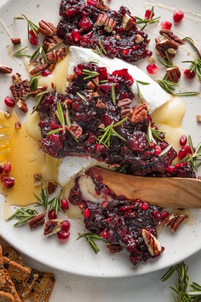 Platter with cranberry pomegranate baked brie and a wooden serving knife scooping up a helping.