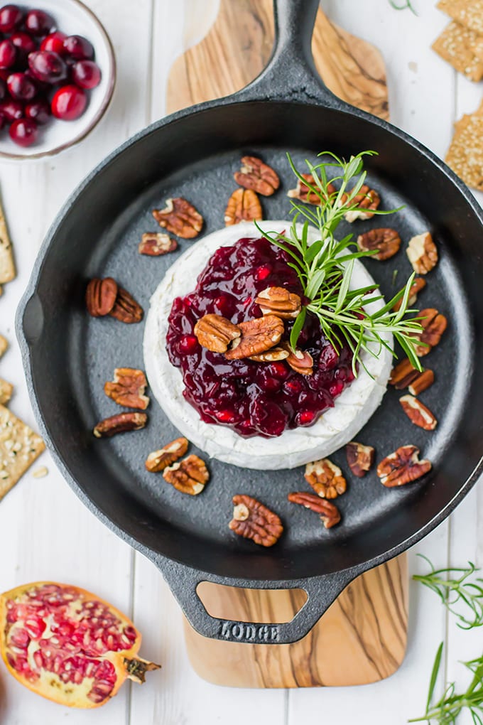 A large wheel of brie baked in a cast-iron skillet, topped with cranberry pomegranate sauce, pecans, and fresh rosemary.