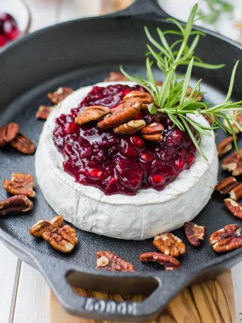 A large wheel of brie baked in a cast-iron skillet, topped with cranberry pomegranate sauce, pecans, and fresh rosemary.
