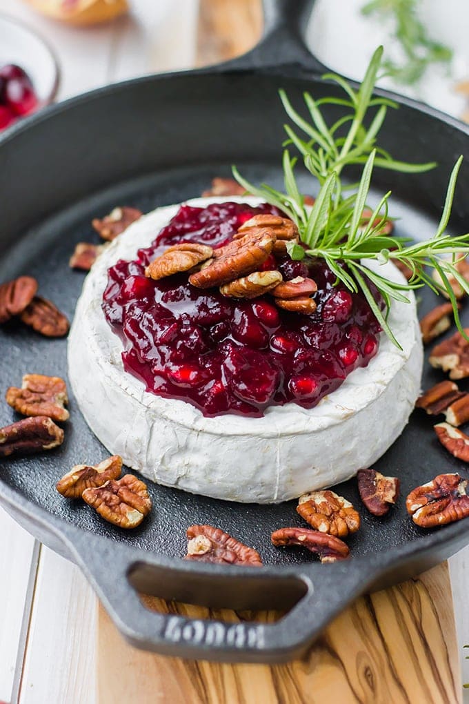 A large wheel of brie baked in a cast-iron skillet, topped with cranberry pomegranate sauce, pecans, and fresh rosemary.