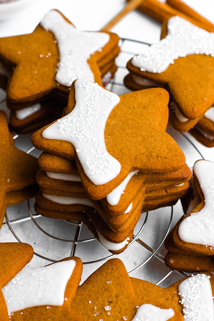 Close-up image of gingerbread cookies cut into a simple five-point star shape, with a pretty crescent of shiny white frosting and sprinkles.