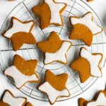 Gingerbread cookies stacked on a cooling rack, with a mug of coffee and cinnamon sticks in the background.