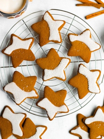 Gingerbread cookies stacked on a cooling rack, with a mug of coffee and cinnamon sticks in the background.