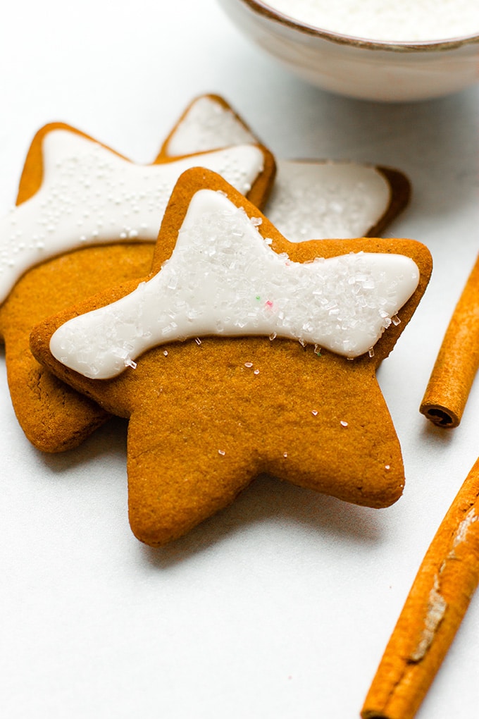 Close-up image of gingerbread cookies cut into a simple five-point star shape, with a pretty crescent of shiny white frosting and sprinkles.