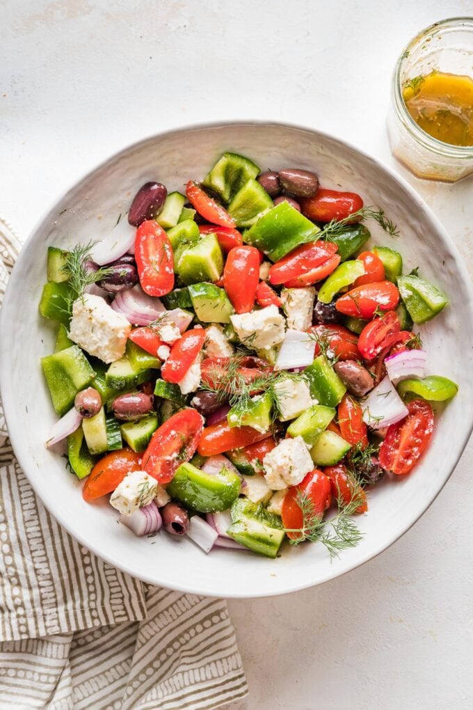 Greek salad ingredients tossed together in a bowl, waiting for dressing.