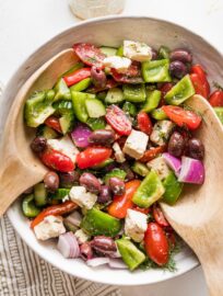 Close up of a large white ceramic bowl holding a Greek salad with homemade dressing.