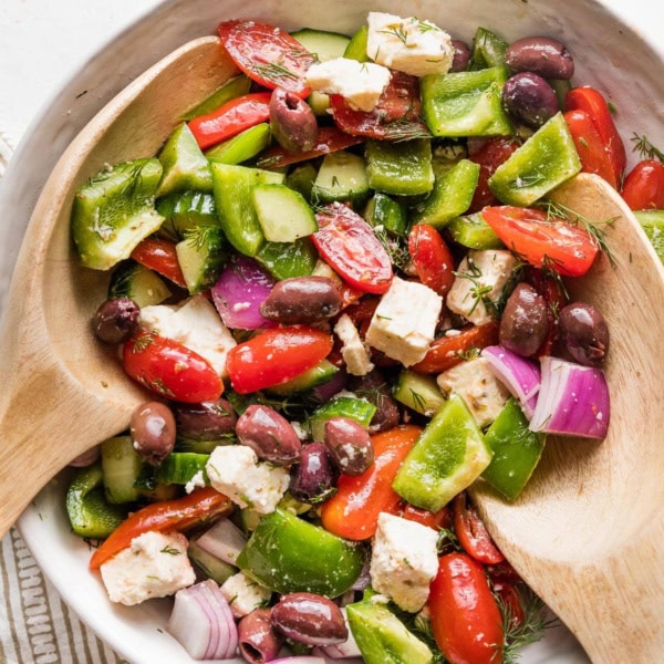Close up of a large white ceramic bowl holding a Greek salad with homemade dressing.