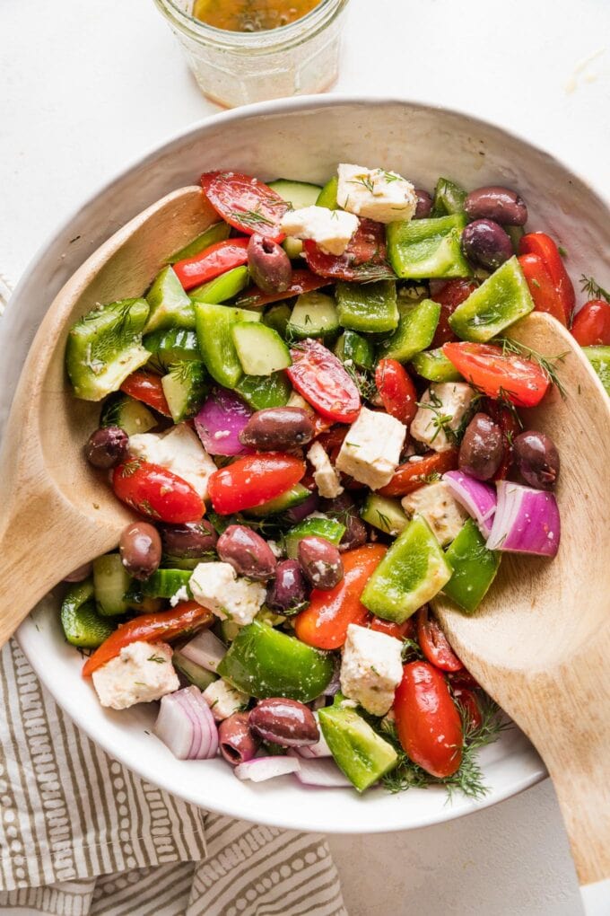 Close up of a large white ceramic bowl holding a Greek salad with homemade dressing.