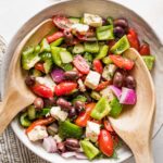 Large white ceramic bowl holding a Greek salad with homemade dressing.