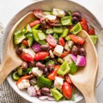 Large white ceramic bowl holding a Greek salad with homemade dressing.